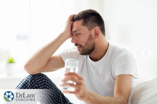 An image of a man man holding his temple with one hand and a glass of water on the other hand